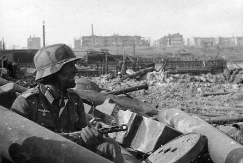 A Wehrmacht Hauptmann of the 6th Army overlooks the city of Stalingrad in a ruined town in 1942. The weapon he's holding appears to be a Captured Soviet PPSH-41 SMG. The Ruined town he's standing today is known as Gagarin Park