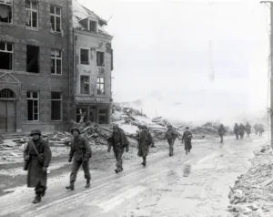 U.S. Inf troops of the 30th Infantry Division on march through Malmedy which was leveled in error by U.S. bombers.