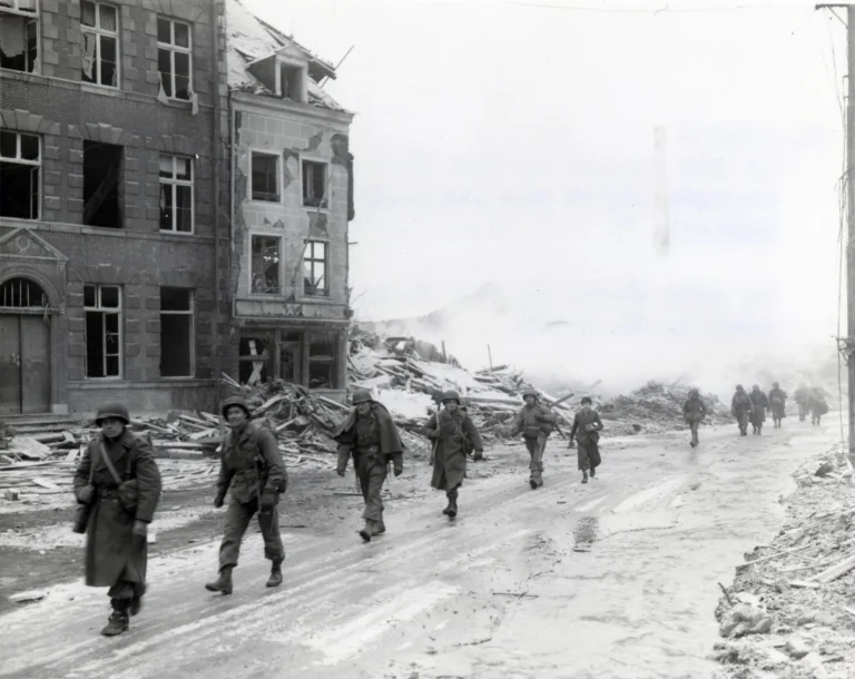 U.S. Inf troops of the 30th Infantry Division on march through Malmedy which was leveled in error by U.S. bombers.