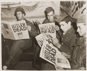 American soldiers read of Hitler's death in an "extra" edition of "Stars and Stripes." Pictured left to right: Pfc. Leonard A. Davis, Pfc. Richard Webster, Pfc. Julian Bellavance, and Pfc. Lex Hall.